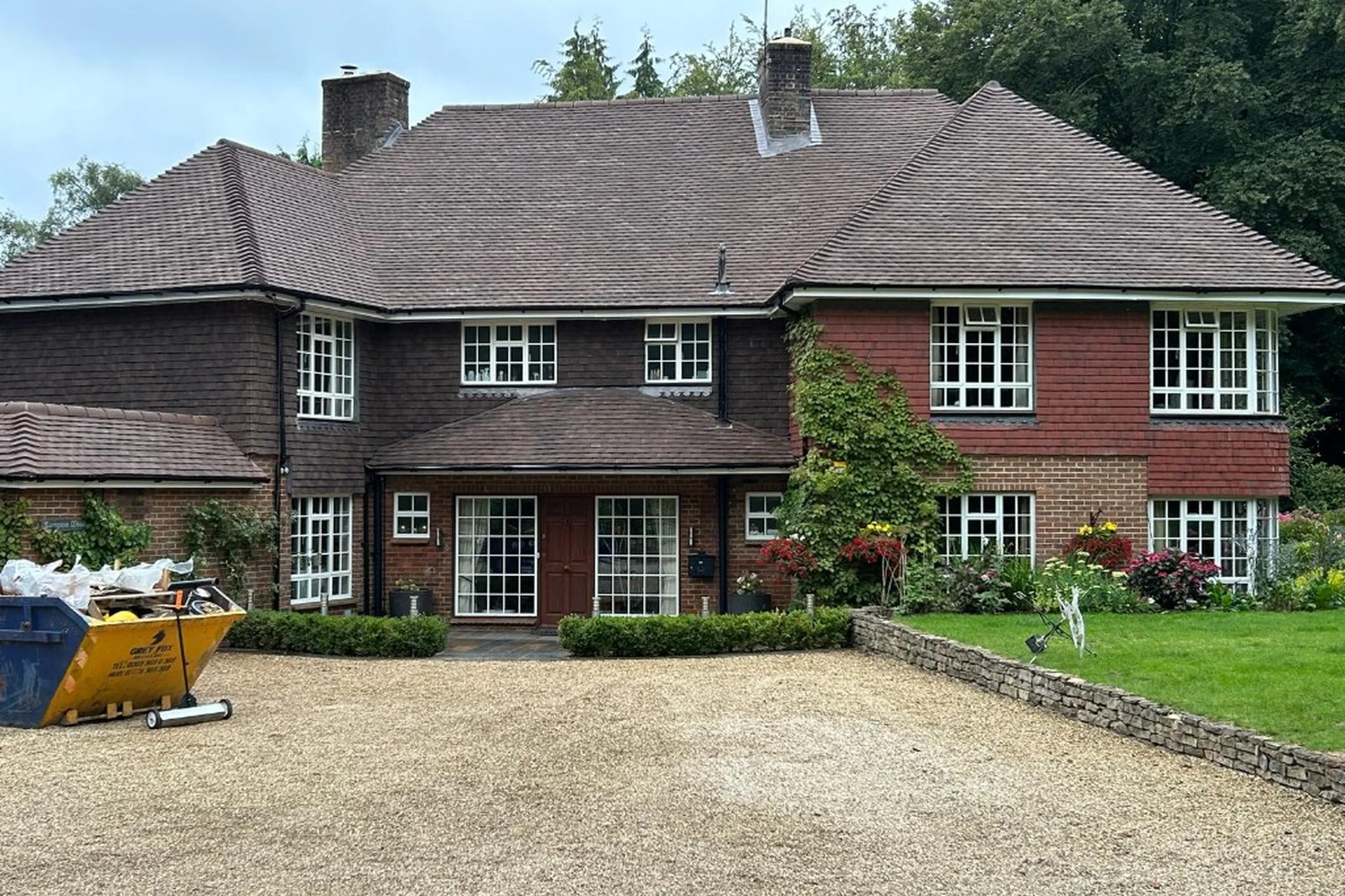 Roofing in Surrey large tile-hung house with multi-gabled dark tiled roof, brick chimneys and gravel driveway in Surrey — Mitchell's Roofing